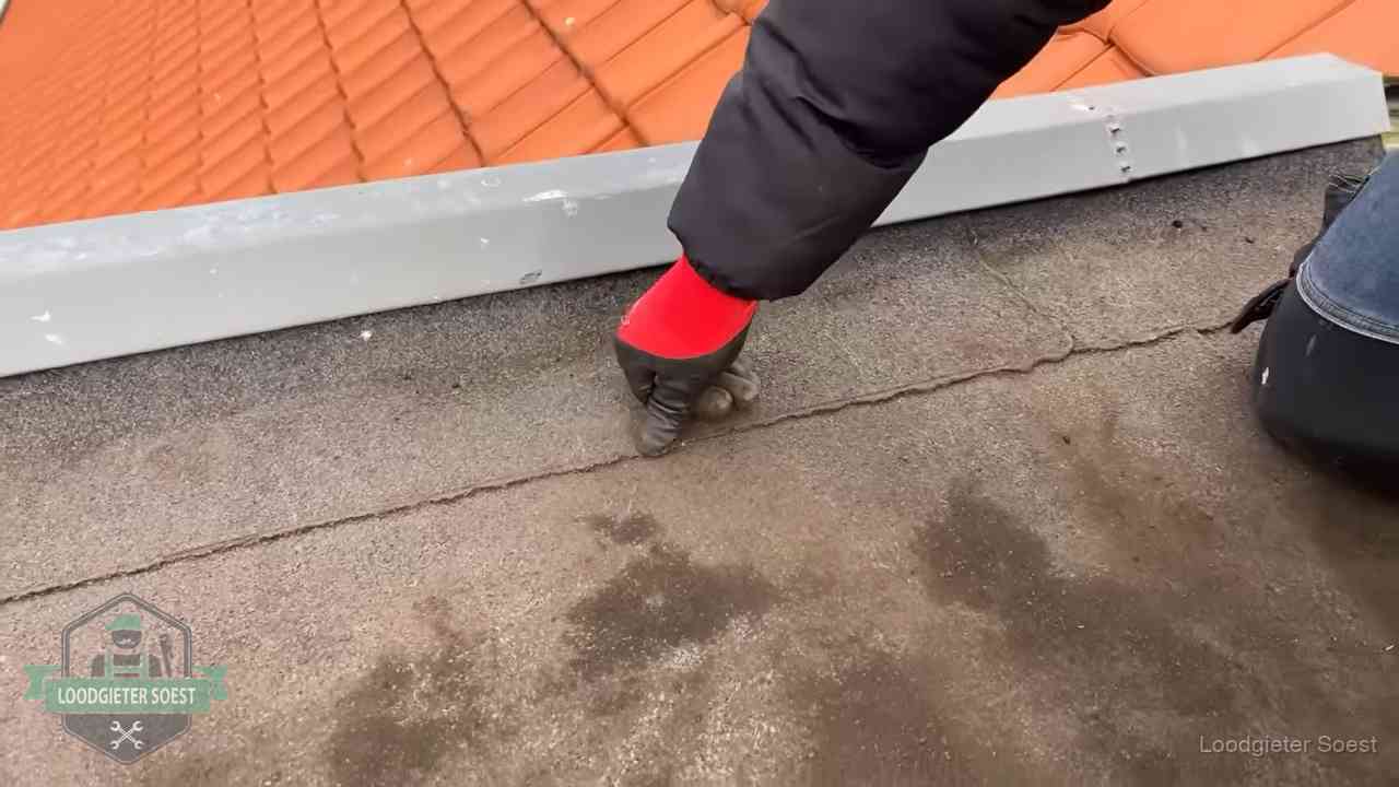 Vakman wijst een naad met vochtplekken aan op een bitumen plat dak in Soest