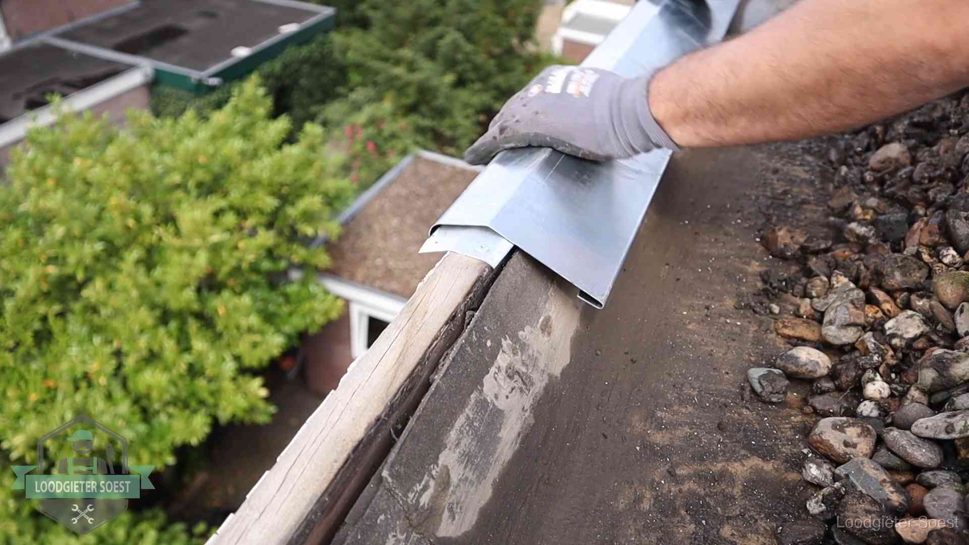 Dakdekker plaatst een zinken deklijst op een dakrand met uitzicht over een woonwijk in Soest