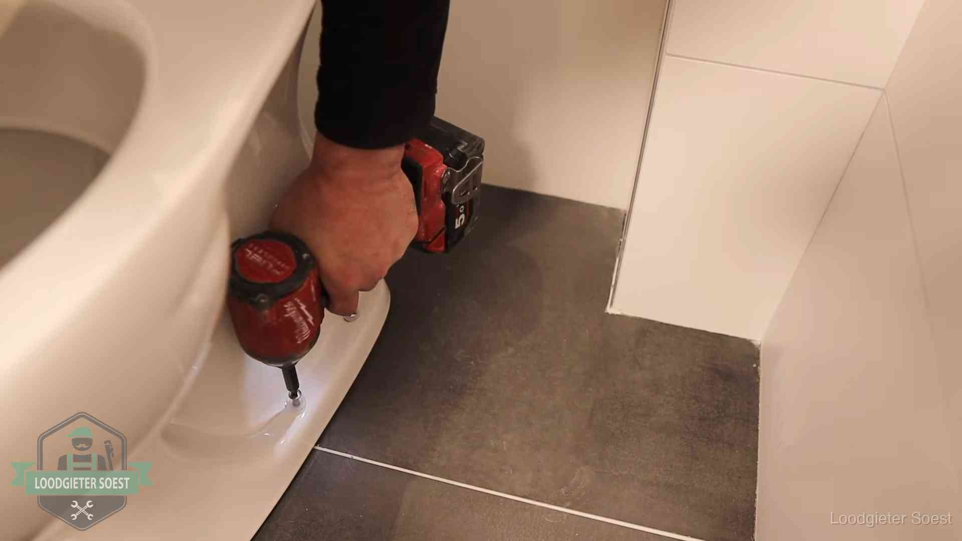 Loodgieter zet de voet van een wc-pot vast op de tegelvloer in Soest